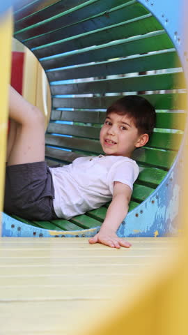 cute kids, boys and girls on playground playing outside.children on slide,in worm tunnel or climbing on rope net.smiling happy kids are having fun.summer day. sstkVertical