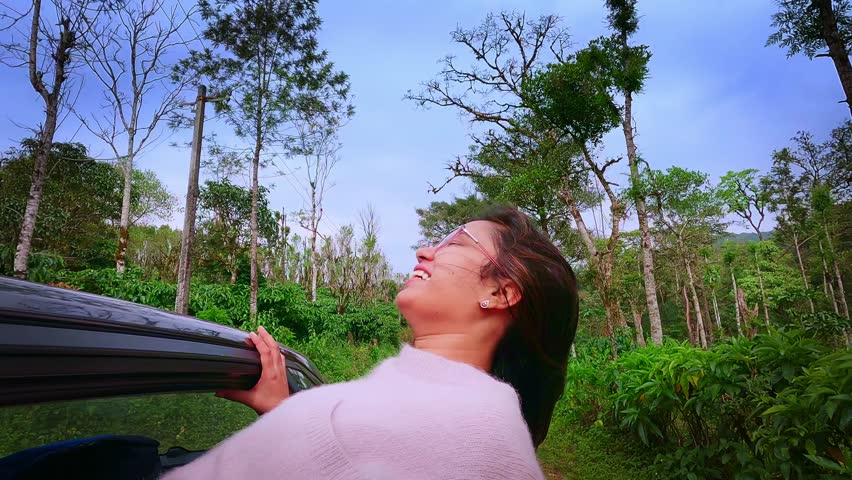 Close-up face of young Indian woman traveling by car while road trip. Woman pulling her face out of car window and enjoying speed while her hair flying away because of the wind. Concept of freedom.	