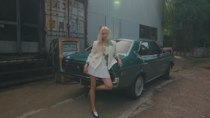 Fashionable woman posing next to a vintage car in front of an industrial building