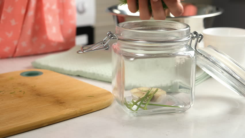 Woman putting dill in glass jar to cook pickles on kitchen, hands close-up. Cuisine, culinary, prepare cook dish, domestic food, recipe, fresh natural organic ingredients concept. Greenery, garlic.