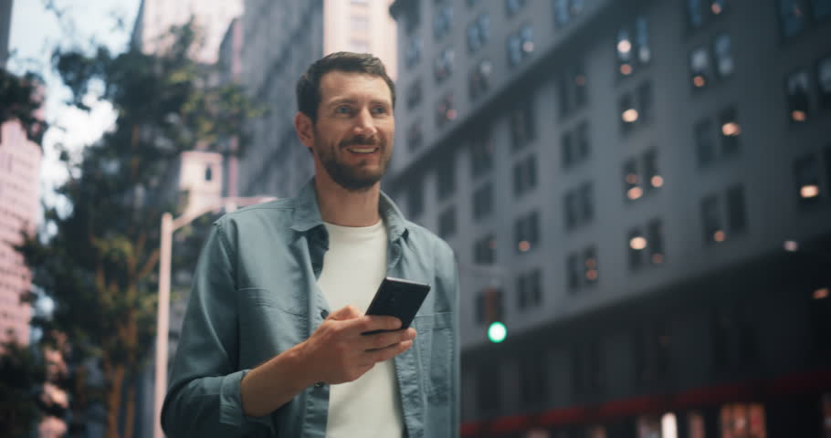Caucasian Man Walking in a Vibrant City, Using a Smartphone for Work, Social Media, and Online Shopping. Tall Buildings Emphasize Urban Connectivity and Digital Interaction, Highlighting Productivity