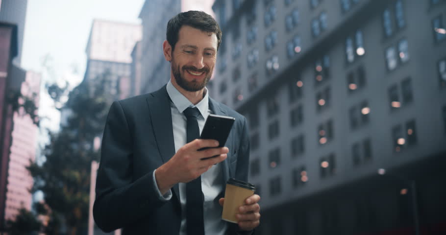 Caucasian Businessman in a Suit Walks Through a Vibrant City, Using a Smartphone for Work, Social Media, and Online Shopping. the Urban Backdrop Emphasizes Digital Connectivity and Productivity