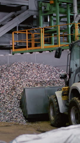 A loader or a Backhoe moves a pile of waste to a garbage factory. A special machine or bulldozer loads garbage at a waste recycling plant. A large pile of plastic and metal, sorting.