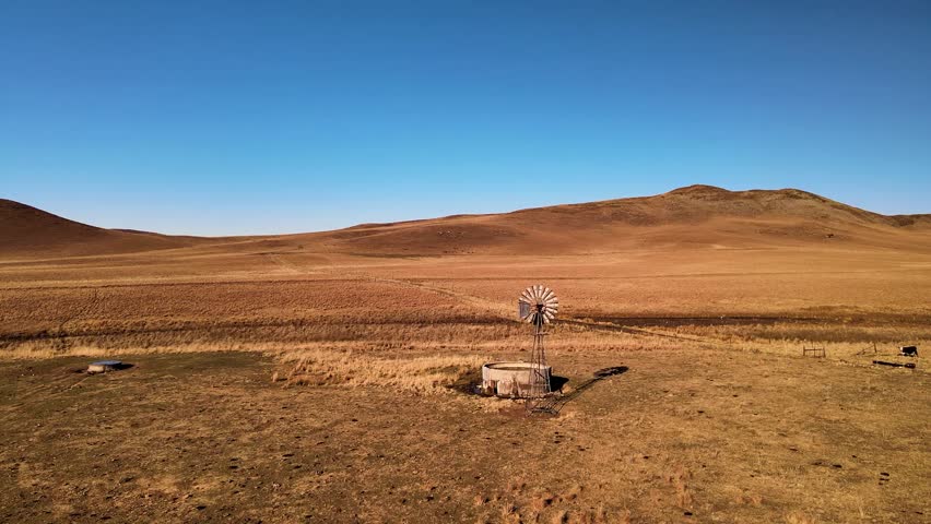 Vast rural farmland, old windmill turning, with a water storage dam under a sunny sky