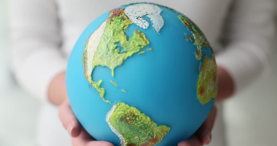 Young woman holds artificial model of Earth in hands. Female demonstrates continents and oceans depicted on small globe model slow motion