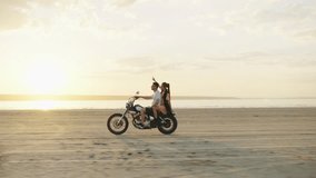 A couple enjoying a motorcycle ride on the beach during a beautiful sunset, embracing adventure, freedom, and romance in the tranquil natural scenery under the colorful sky - Powered by Shutterstock - Get 15% off with code: PIKWIZARD15