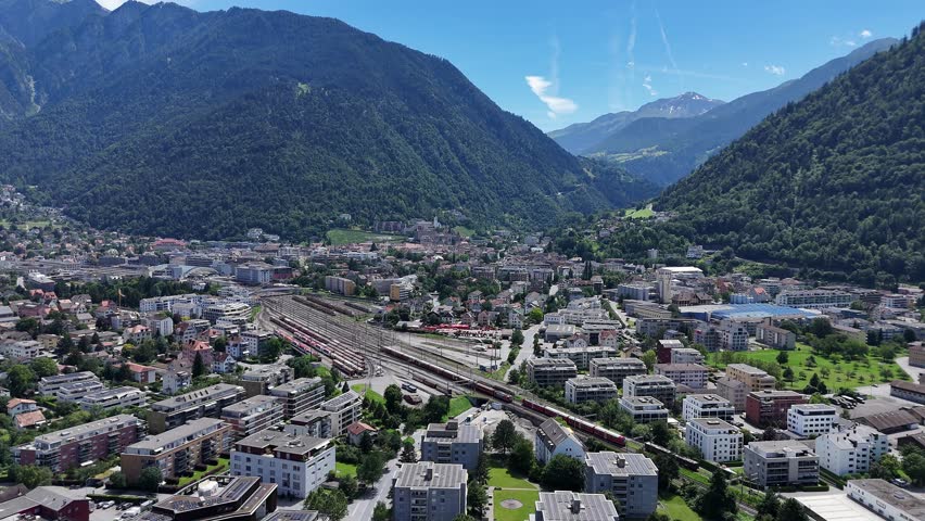 Chur Town with housing area and train station with tracks in Switzerland. Green mountain range against blue sky in summer. Wide shot. Switzerland, Europe.