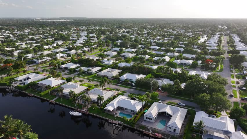Drone footage of a suburban waterfront community in Florida. White-roofed homes, lush greenery, and boats on a canal. Residential area, aerial.
