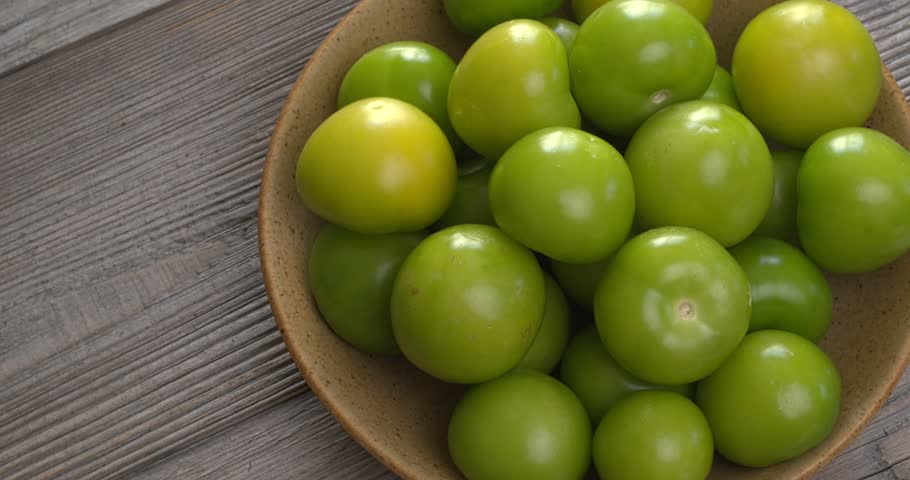 A heap of husked tomatillo in a bowl on rustic wooden table. Copy space, table spin.
