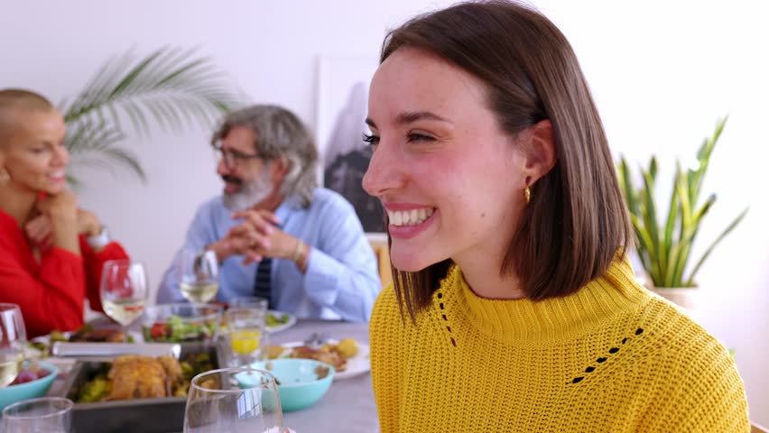 Happy young woman enjoying dinner party with family at home. Side view portrait of cheerful beautiful female drinkin white wine sitting on table