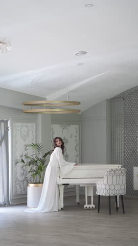 A young beautiful woman is posing near a white grand piano in an elite establishment. The concept of advertising a wedding dress, underwear or wedding matinee.