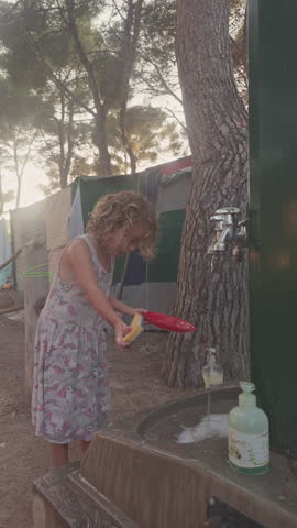 cool small girl washing dishes in a campsite in vertical