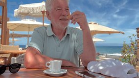 Handsome smiling senior man sitting outdoors at cafe table at sea drinking an espresso coffee cup eating a little cookie, elderly white haired bearded male enjoying relax in a beautiful sunny day - Powered by Shutterstock - Get 15% off with code: PIKWIZARD15