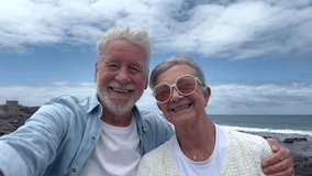 Happy smiling senior couple in vacation at sea admiring the seascape and the ocean waves. Elderly man takes photos for memory with phone, horizon over water - Powered by Shutterstock - Get 15% off with code: PIKWIZARD15