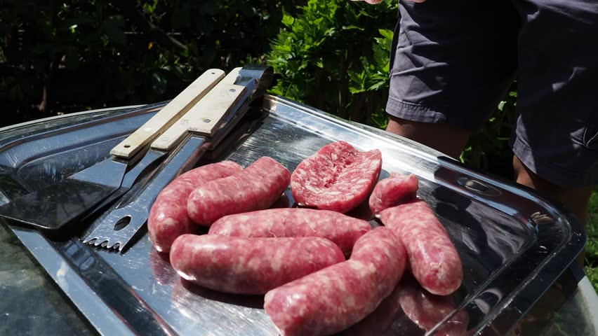 Man cuts sausages for barbecue. Sunday lunch outdoors. Outdoors activity. Family concept