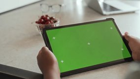 African American boy is holding in hands and using tablet pad with green screen chroma key display and motion trackers, sitting at table - Powered by Shutterstock - Get 15% off with code: PIKWIZARD15
