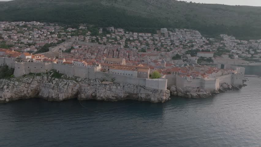 Panoramic aerial video of picturesque town of Dubrovnik in Croatia at morning light, old town with red roofs and narrow streets surrounded by ancient city walls on Adriatic sea coast.