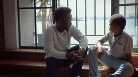 African American father and son sitting together near window talking. Black skinned man and boy chatting heartfelt conversation - Powered by Shutterstock - Get 15% off with code: PIKWIZARD15