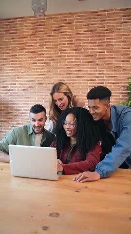 Vertical Group of young adult friends having fun using a laptop sharing on the social media. Happy multiracial people browsing online with a computer. Couples watching videos with a notebook at home