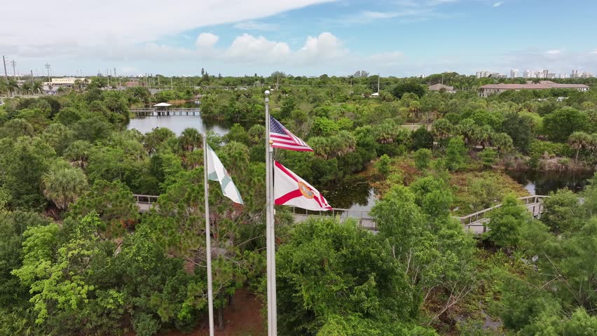 American and Florida Flag waving in Country Club with green trees and river of Naples. USA. Aerial orbit shot.