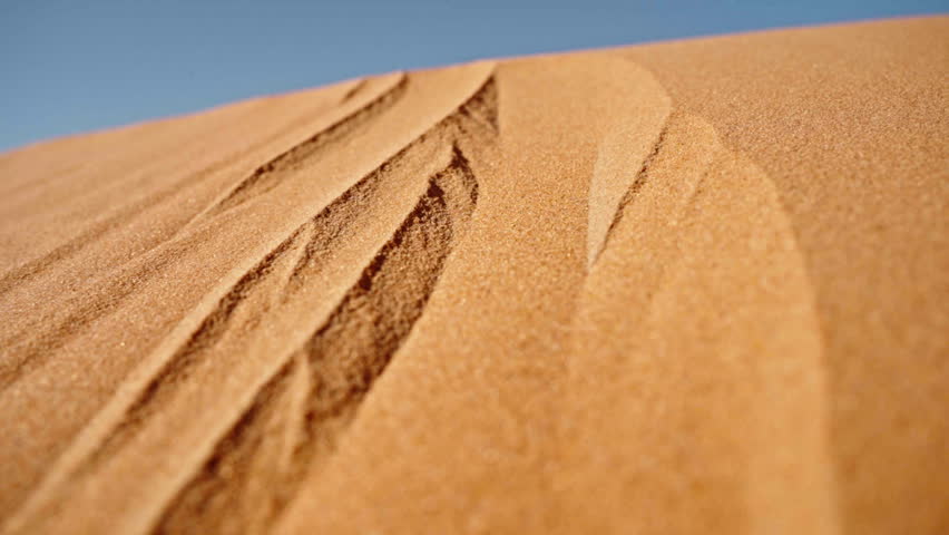 Golden sand dunes with intricate patterns under a clear blue sky