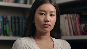 Serious concentrated asian woman girl student teenager businesswoman business lady teacher customer nod head approve agree looking at camera with piercing stern gaze posing indoors near bookshelf - Powered by Shutterstock - Get 15% off with code: PIKWIZARD15