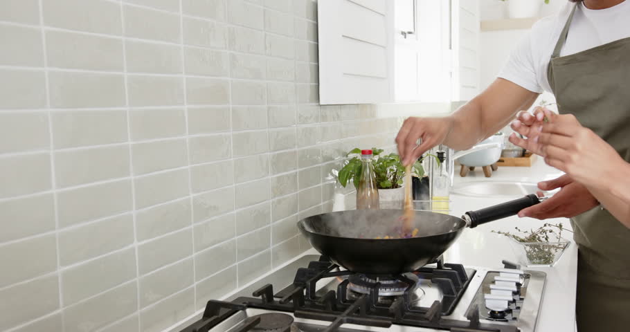 Lifestyle videos indoor of people doing activities at home, cooking together, couple adding spices to stir-fry in modern kitchen. cooking, picking up ingredients and adding to a pan