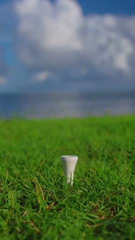 Golfer placing golf ball on the tee at golf course. Close up. Male hand in a golf glove puts the ball on the field on the background of the blue ocean