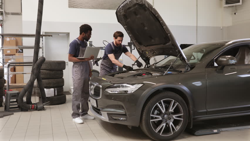Two auto mechanics inspecting car engine in workshop environment. Professionals diagnosing vehicle with laptop and tools. Automotive maintenance, repair, and teamwork concept - Powered by Shutterstock - Get 15% off with code: PIKWIZARD15