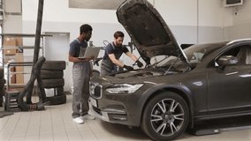 Two auto mechanics inspecting car engine in workshop environment. Professionals diagnosing vehicle with laptop and tools. Automotive maintenance, repair, and teamwork concept - Powered by Shutterstock - Get 15% off with code: PIKWIZARD15