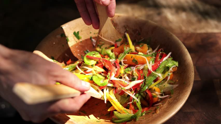 Closeup of hands tossing a fresh salad in a wooden bowl