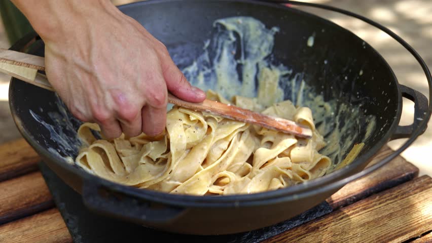 Close-up shot of chef twirling pasta in a creamy sauce outdoors, perfect for food and cooking videos.