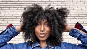 Confident woman flaunts trendy look with afro hairstyle and denim jacket against brick wall backdrop - Powered by Shutterstock - Get 15% off with code: PIKWIZARD15