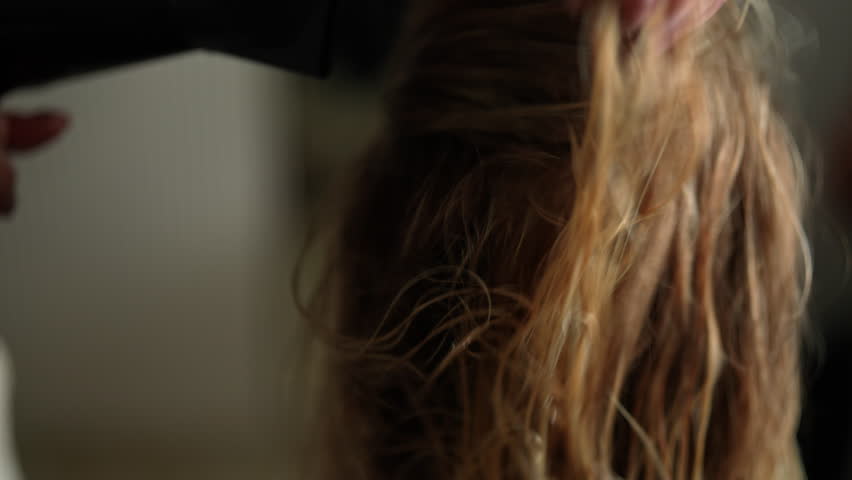 Closeup of female hairdresser accurate drying wet long blonde hair of young woman customer with hairdryer in beauty studio. Lady client getting stylish hairdo done at salon. Shooting in slow motion.
