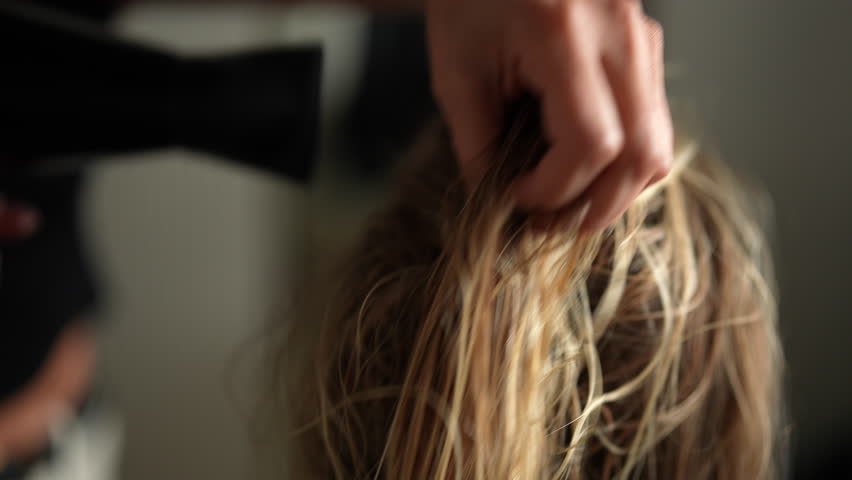 Closeup of female hairdresser accurate drying wet long blonde hair of young woman customer with hairdryer in beauty studio. Lady client getting stylish hairdo done at salon. Shooting in slow motion.