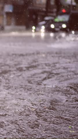 Vertical video, Slow motion, Swift stream of rainwater flows into storm drain, cars are driving at city crossroads on background, panorama. Heavy rain leads to sewage overflow, flood in city