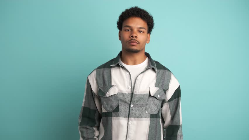 Serious young man looking at camera in blue studio