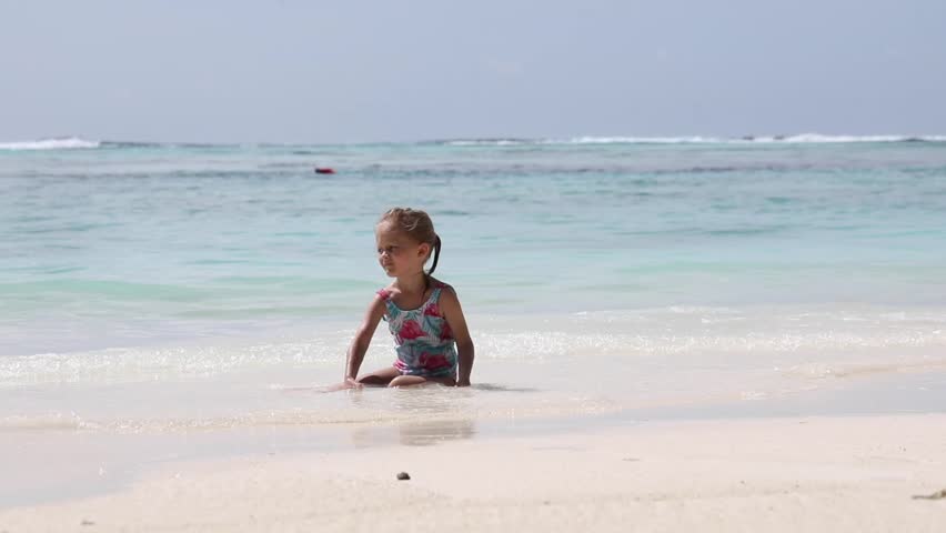 girl swims in the ocean, child sits on the sand and plays with water and sand, white sand, exotic vacation on the island