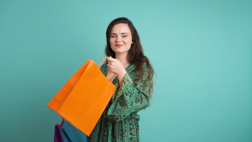Happy woman showing shopping bags in blue studio