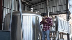 A Man tasting craft beer In the back is a large brewery with the concept of making your own craft beer. - Powered by Shutterstock - Get 15% off with code: PIKWIZARD15