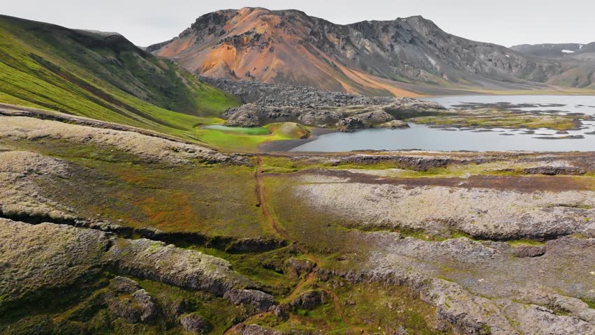 Flying over the lake, colored rhyolite mountains and frozen lava in Landmannalaugar, Iceland. Landmannalaugar hiking area located in the center of the island and is part of Fjallabak Nature Reserve