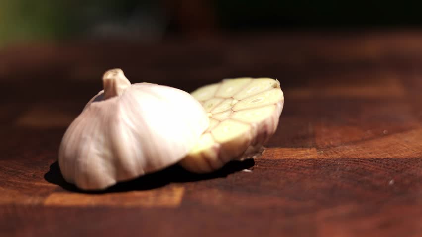 A garlic bulb is cut in half, revealing the cloves inside, resting on a wooden cutting board.