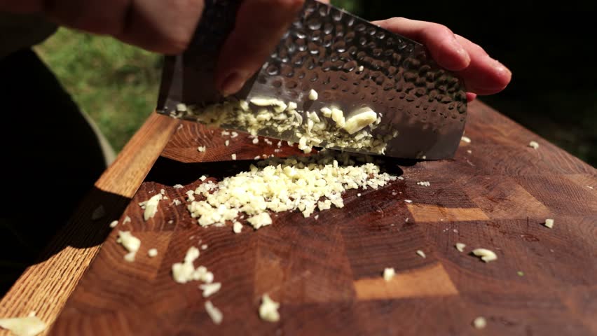 Close-up shot of chopping garlic cloves on a wood cutting board for food preparation.