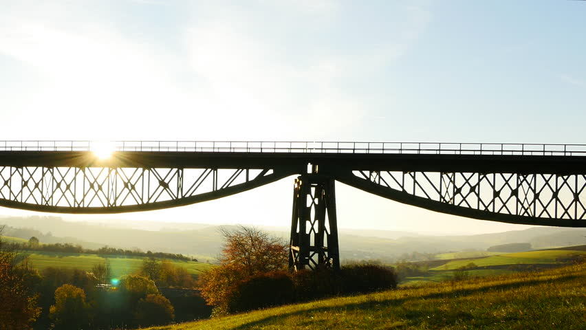 Vintage steam train crossing a bridge at sunset with beautiful views of hills and nature