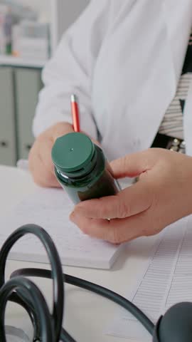 Vertical Screen: Doctor holding pill bottle and writing dosage on it. Nurse analyses doctor prescriptioned capsules.