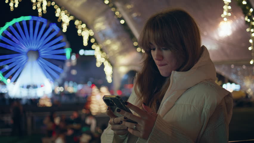 Girl taking photo ferris wheel on cellphone at night festive amusement fair closeup. Woman capturing holiday lights on smartphone at luna park. Happy lady photographing evening illuminated fairground.