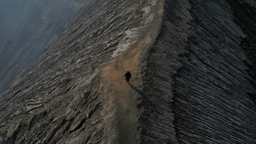 Man walking cliff volcano crater Bromo drone view