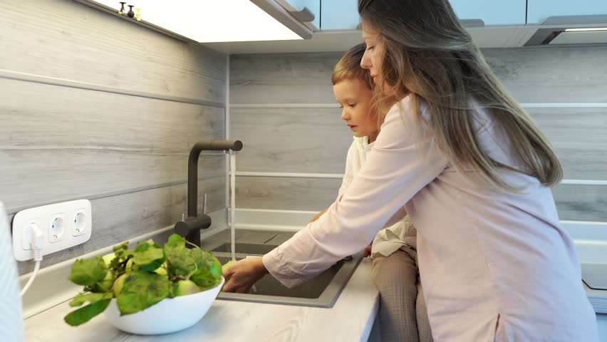 little boy sitting and washing apples in the sink