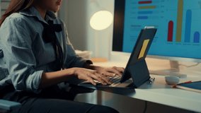Businesswoman analyzes data on a laptop while referencing charts on a desktop screen in a modern office. Working late with professional focus - Powered by Shutterstock - Get 15% off with code: PIKWIZARD15