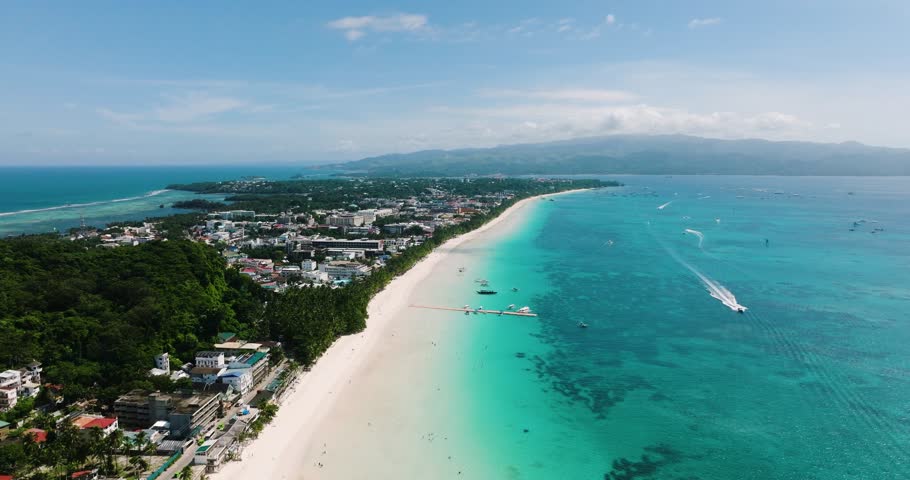 Powdery white sand beach with waves and boats running over the turquoise sea water. Boracay Island. Philippines.
